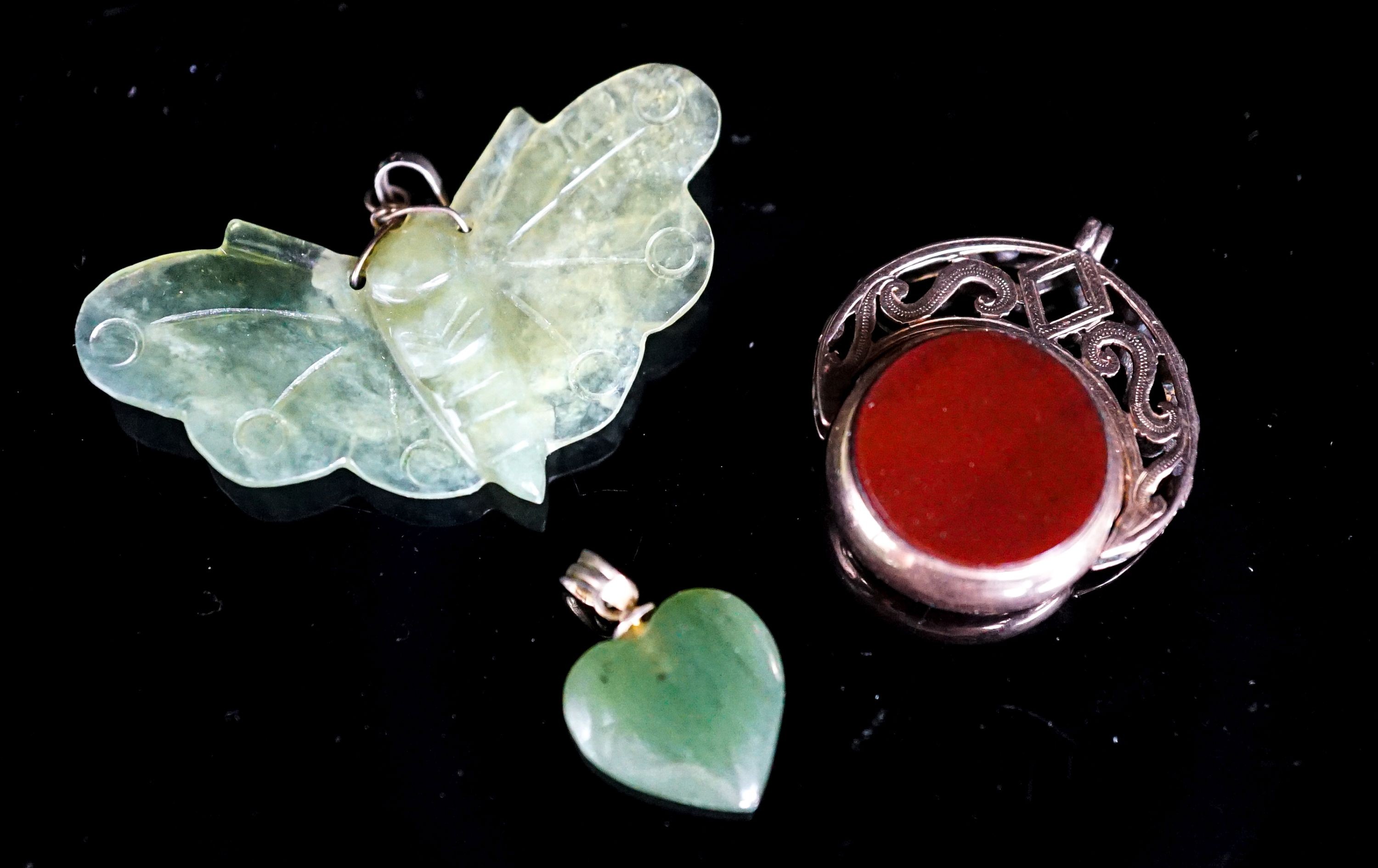 A nephrite moth pendant, 46mm, a similar heart pendant and a yellow metal mounted chalcedony spinning fob seal.